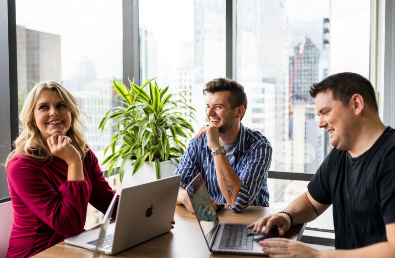 Three people at an office table smiling and talking.