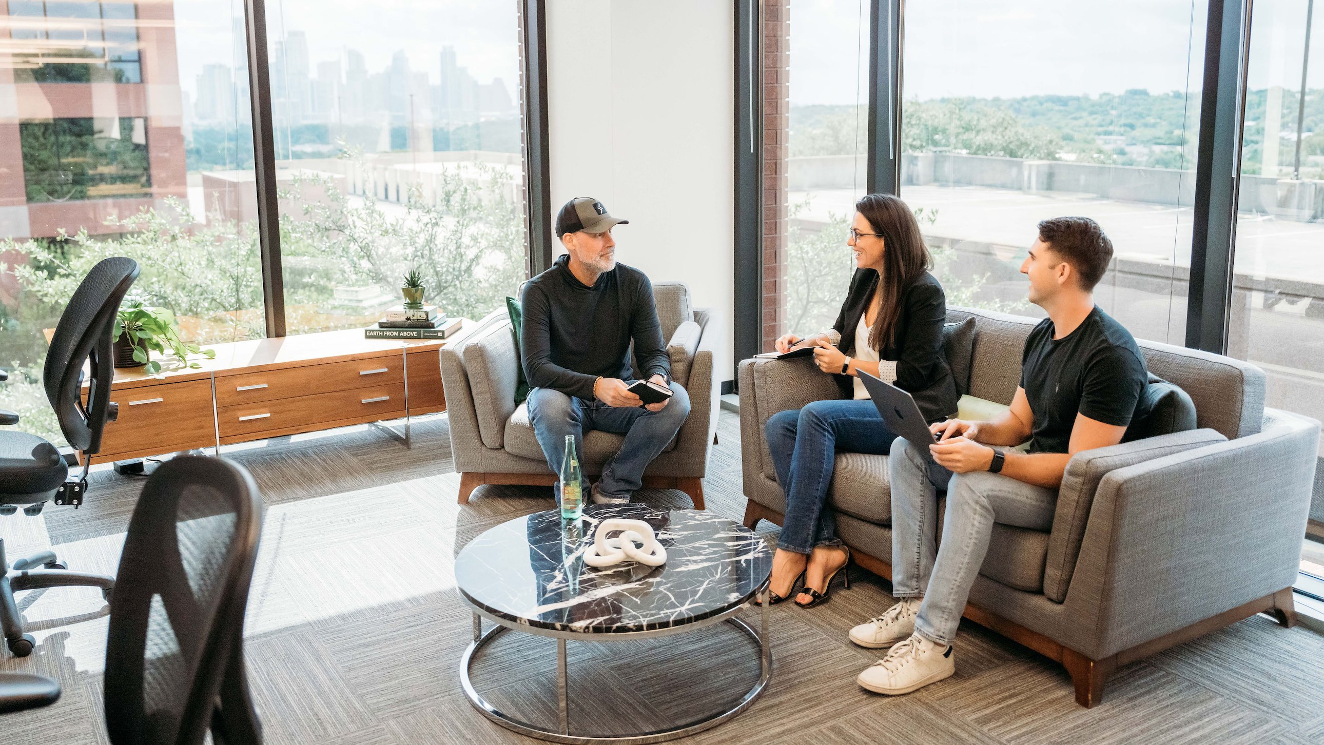 Three Scorability team members sit in a lounge area, meeting with notebooks and a laptop handy.