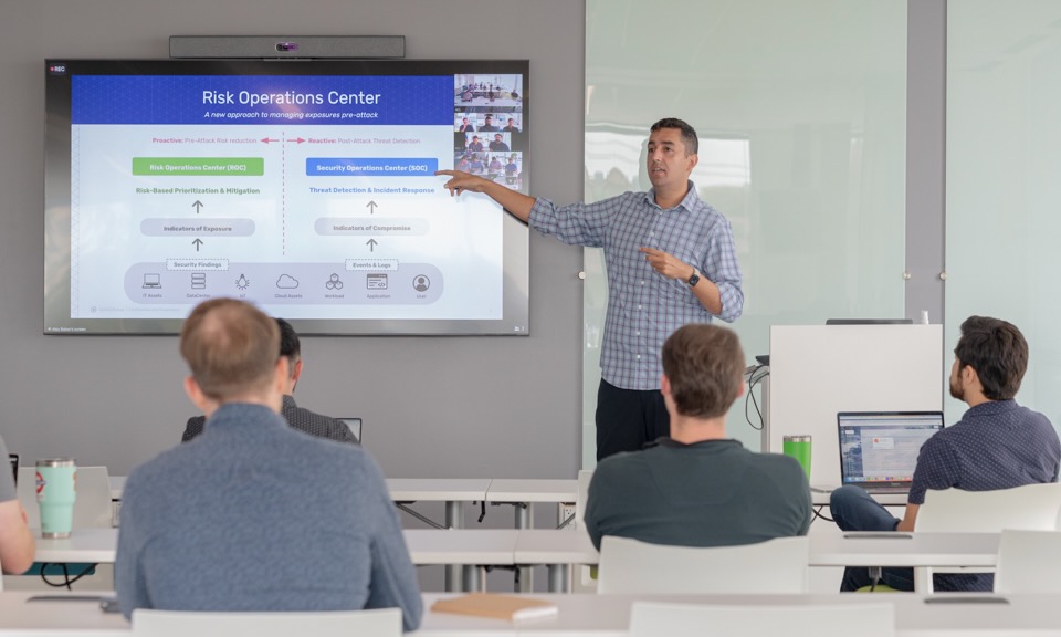 Alex Babar presents at a screen in front of a room of Brinqa coworkers